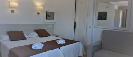 Habitación de hotel con dos camas, un sofá, un espejo y lámparas fijadas a la pared.