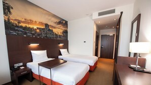 Une chambre d’hôtel avec deux lits, un bureau, une table de chevet, une lampe et une fresque murale.