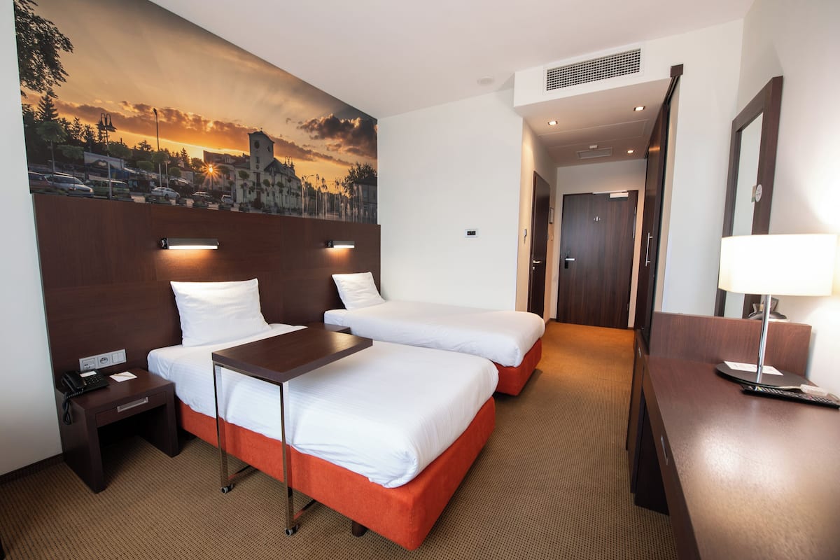 Habitación de hotel con dos camas, un escritorio, una mesita de noche, una lámpara y un mural en la pared.