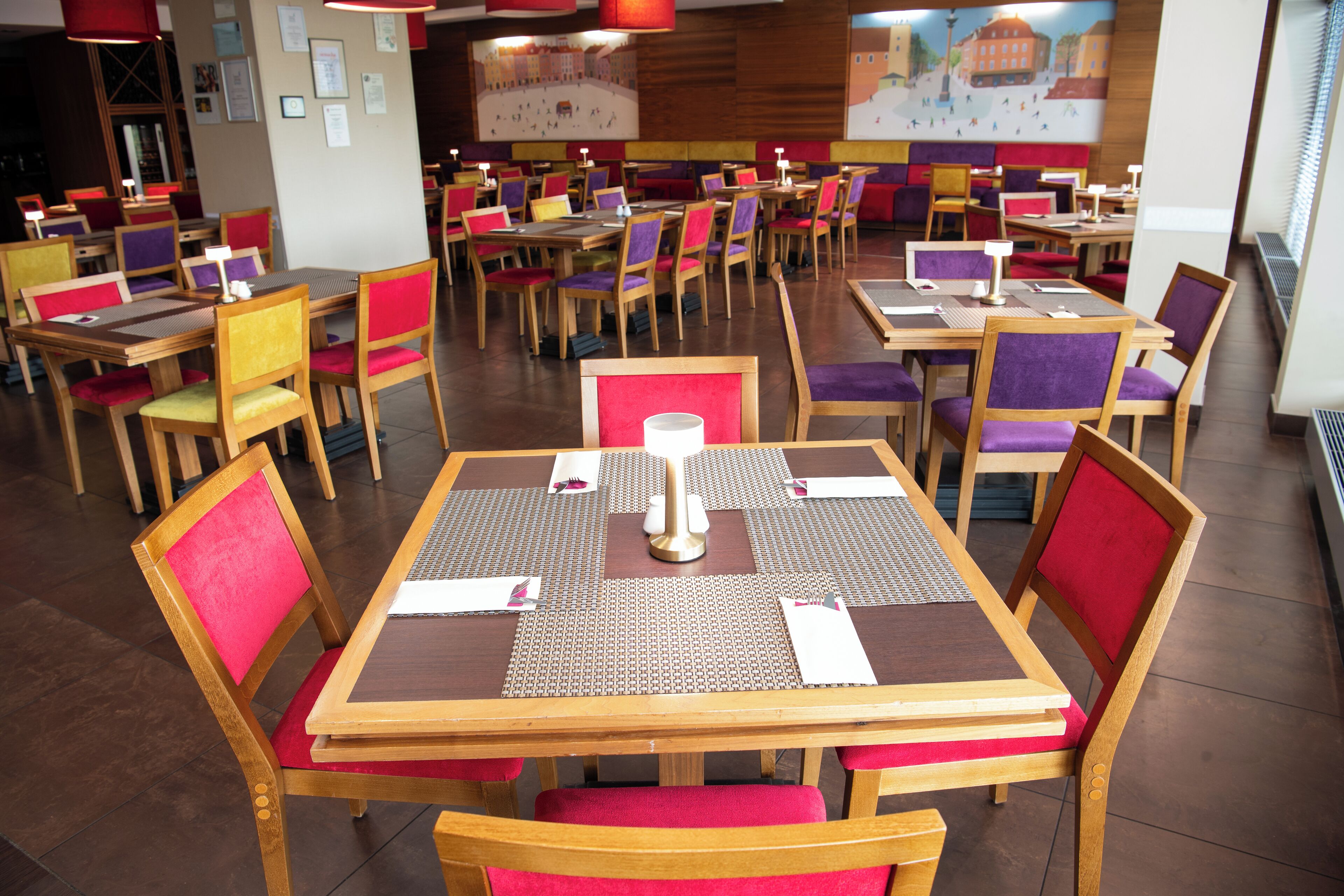 Un restaurant avec de nombreuses tables et chaises, chacune étant agrémentée d’un set de table et d’une serviette blanche.