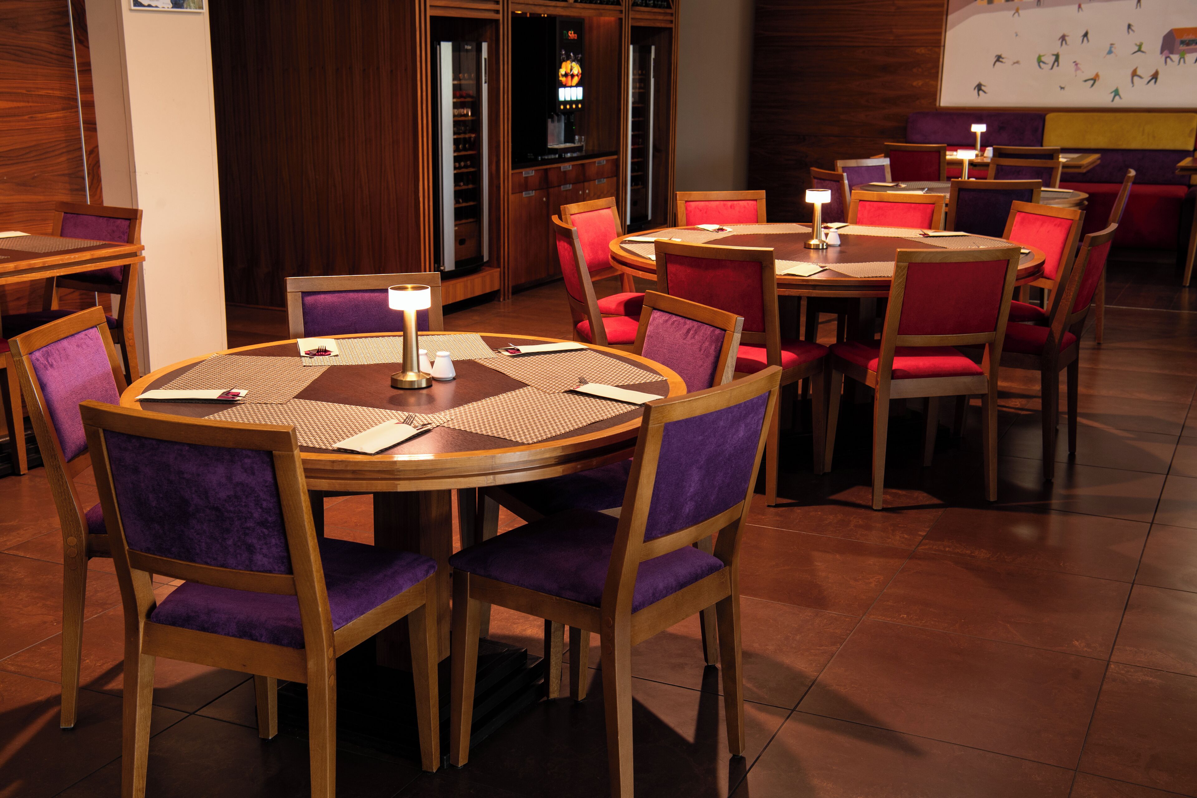 Un ristorante con tavoli rotondi e sedie imbottite viola, caratterizzato da un interno in legno e pavimento piastrellato.