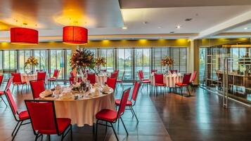 A spacious dining area with round tables, red chairs, and large windows providing a view of the outdoors.