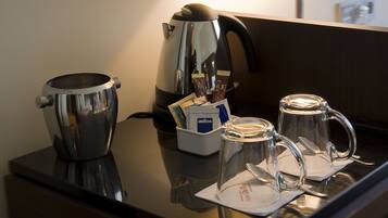 Un coin café équipé d’une bouilloire, de tasses à café et d’un récipient contenant des capsules de café.