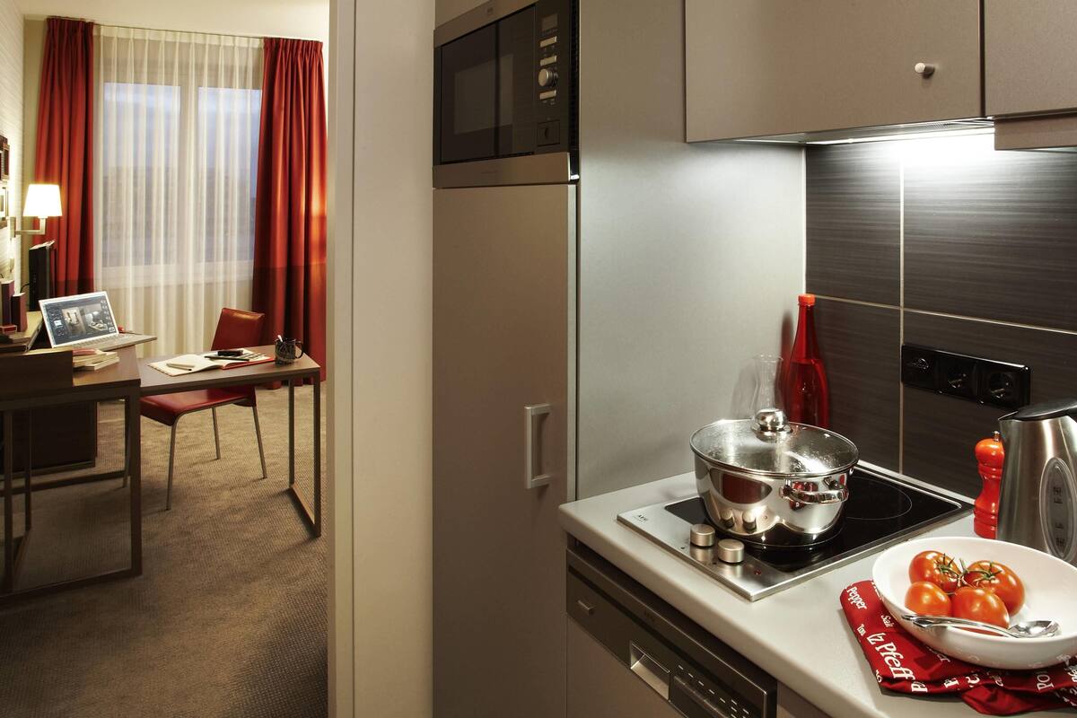 A modern kitchen with stainless steel appliances, a dining area with a table and chairs, and a view of a room with curtains.