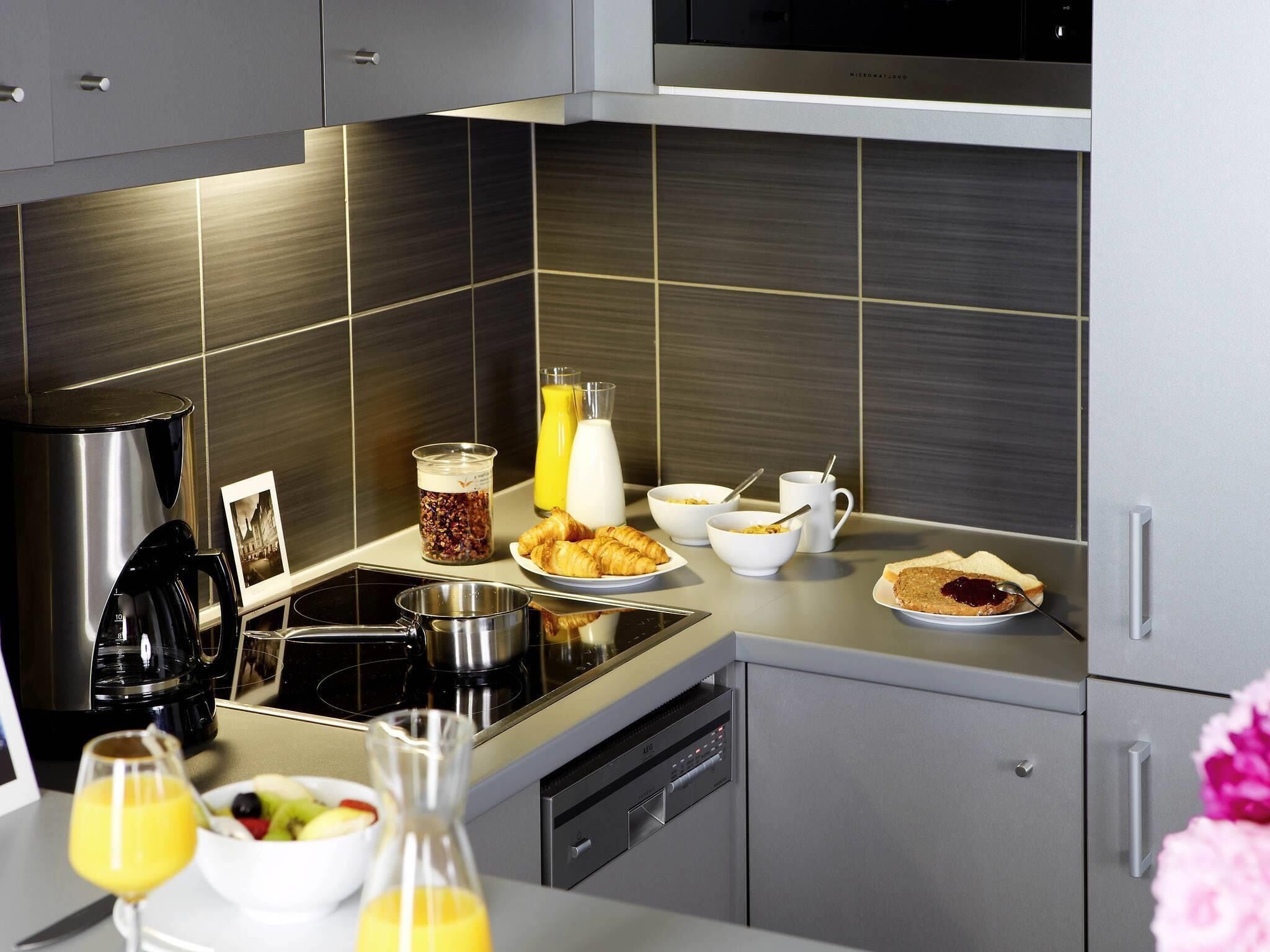 A modern kitchen with stainless steel appliances, a coffee maker, a kettle, and breakfast items on the counter.