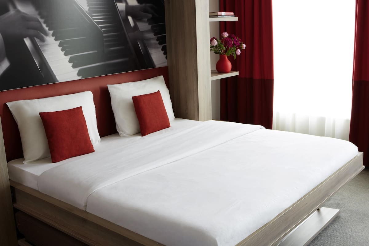 Una cama con ropa de cama blanca y roja, un cabecero rojo y un jarrón con flores sobre una estantería.