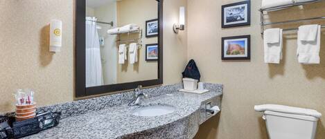 A bathroom with a granite countertop sink, a large mirror, a towel rack with towels, and a toilet.
