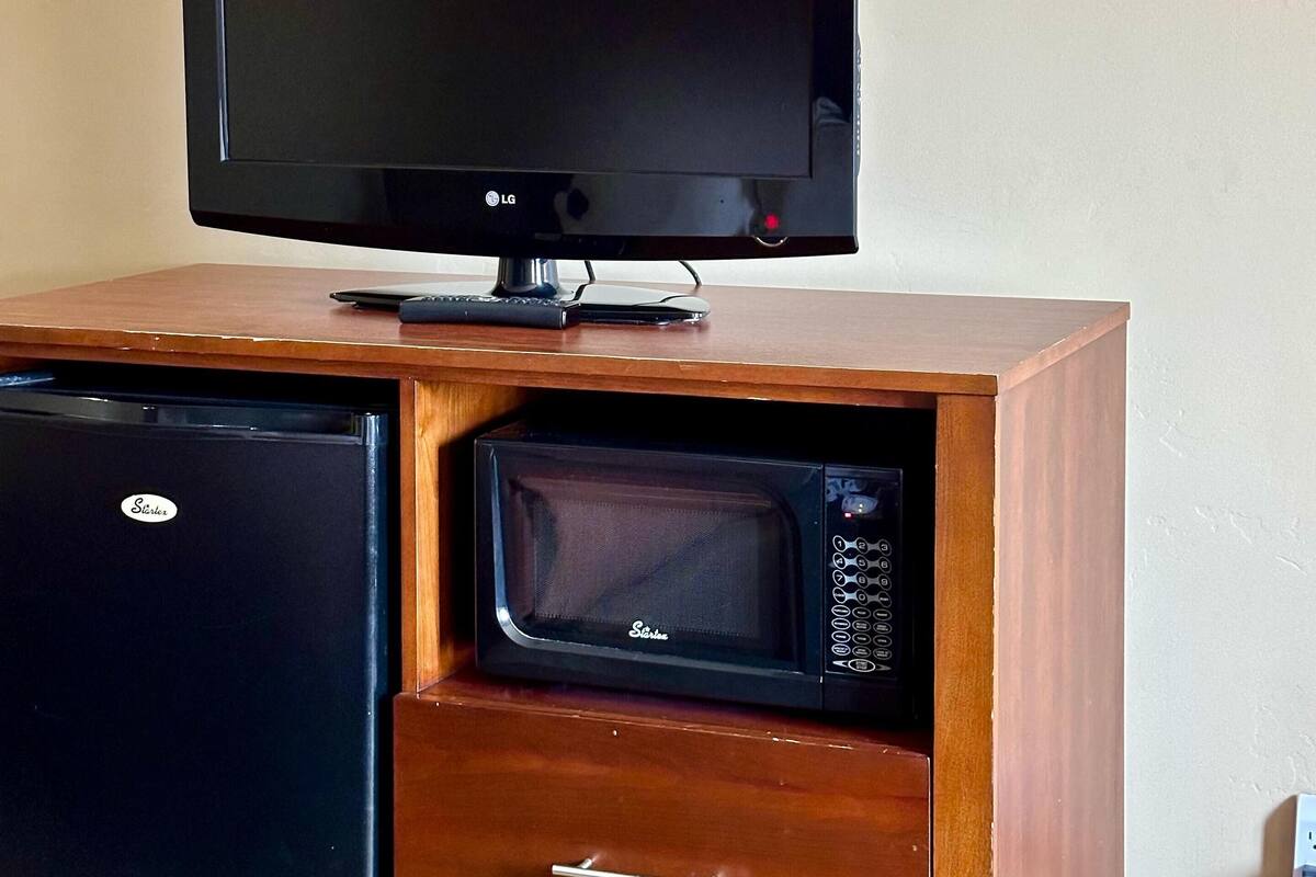 A wooden cabinet with a television, a microwave, and a refrigerator.