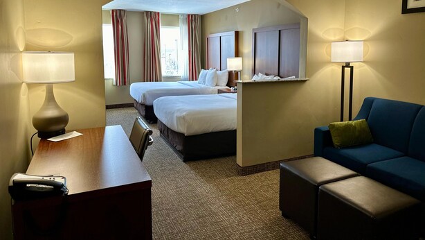 A hotel room with two beds, a desk, a chair, a sofa, and a standing lamp.