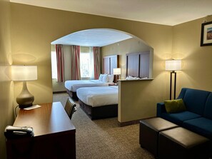 Hotellihuone, jossa on kaksi sänkyä, työpöytä, tuoli, sohva ja lattiavalaisin.