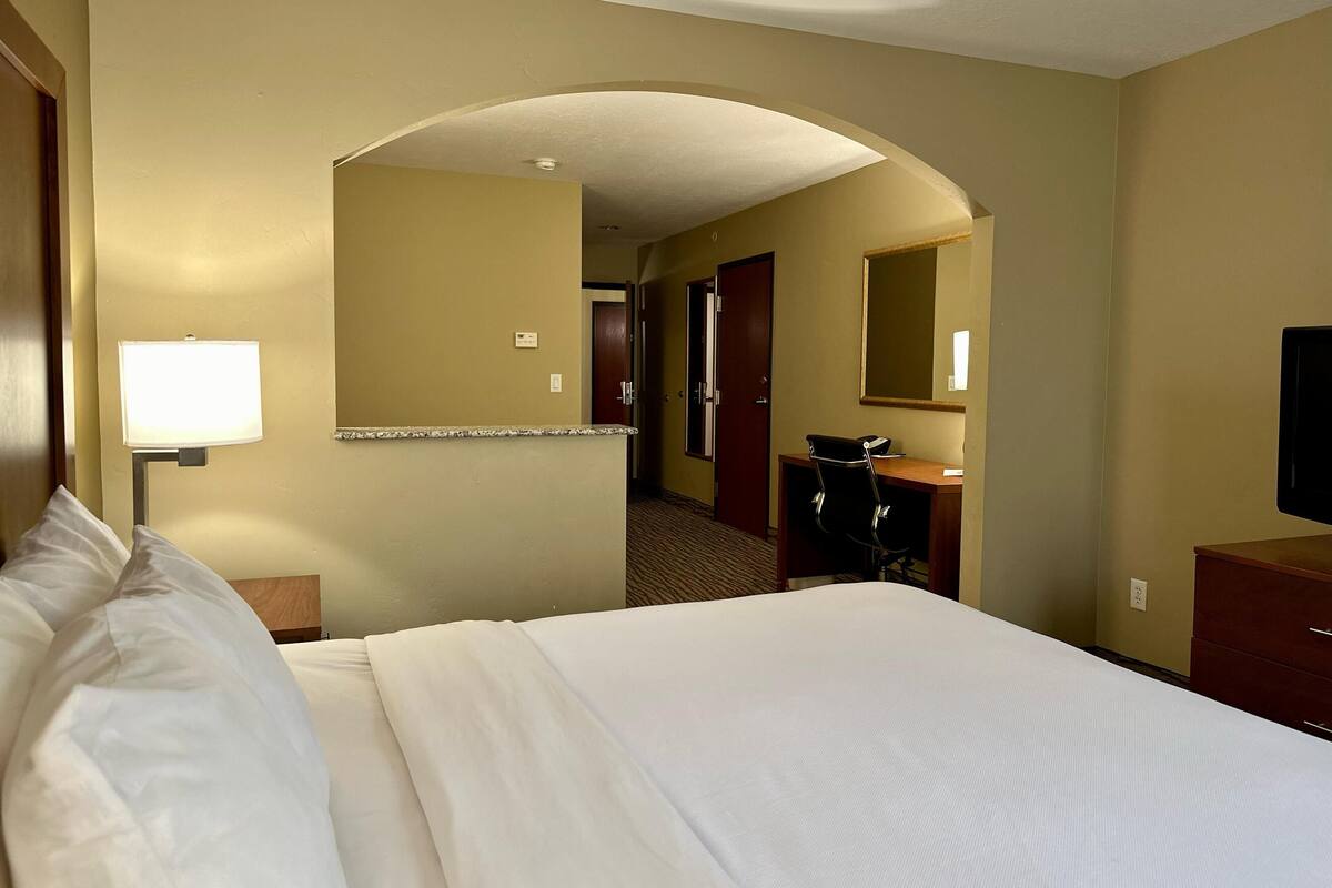 A hotel room with a bed, a desk, a chair, a desk lamp, a mirror, and a television.