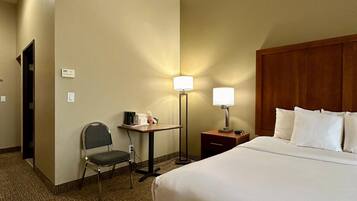 Una habitación de hotel con una cama grande, un escritorio con una silla, una lámpara y una pequeña mesa con una cafetera.