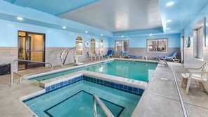 An indoor swimming pool with clear water, blue and white tiled walls, and several lounge chairs.