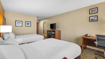 A hotel room with two beds, a desk, a chair, a TV, and a lamp.