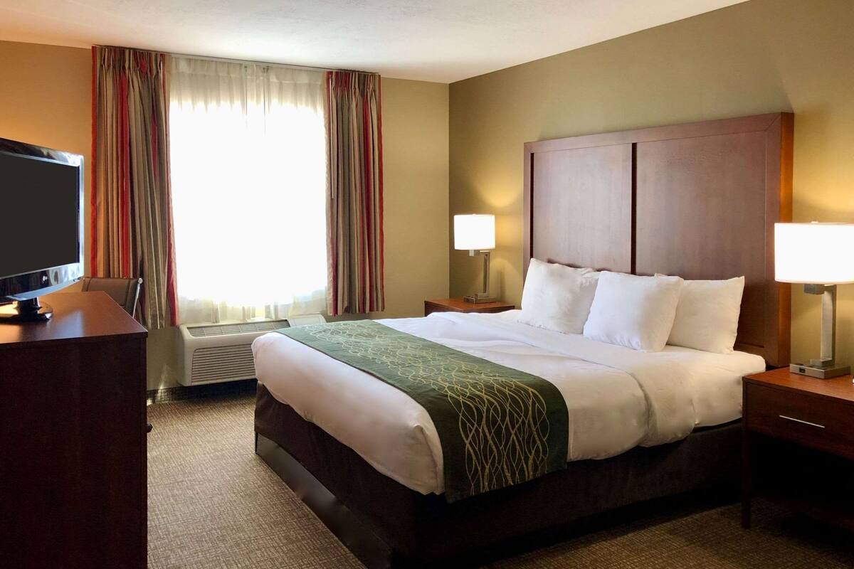 A hotel room with a bed, a desk with a TV, two bedside lamps, and a window with curtains.