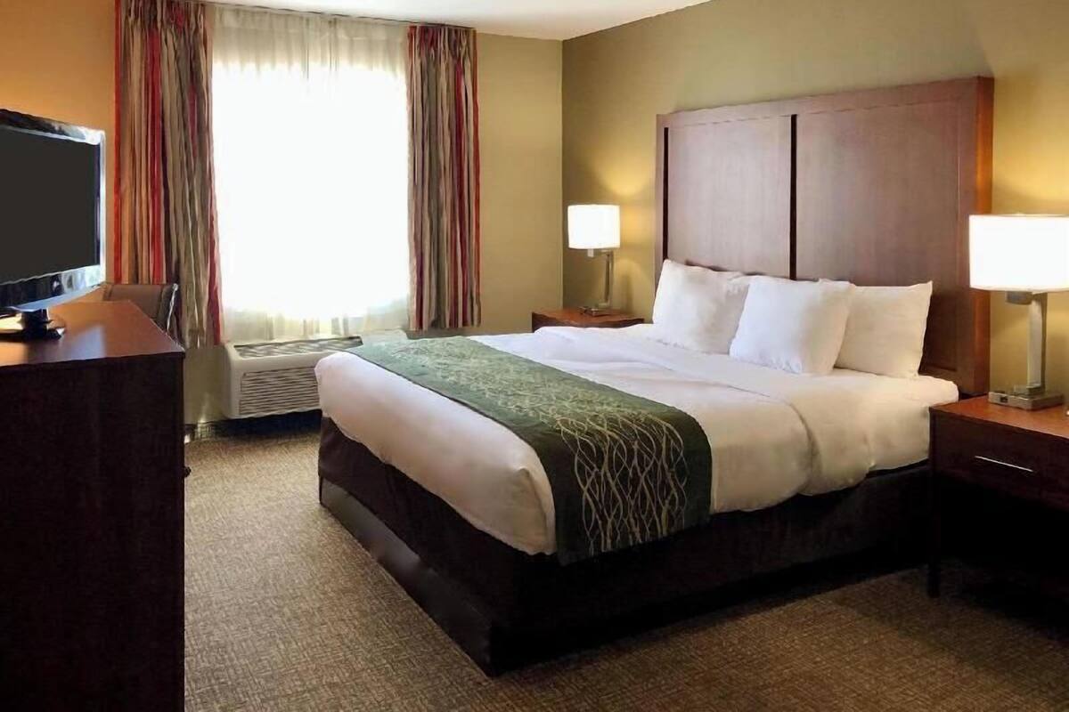 A hotel room with a bed, two bedside lamps, a desk with a television, and a window with curtains.