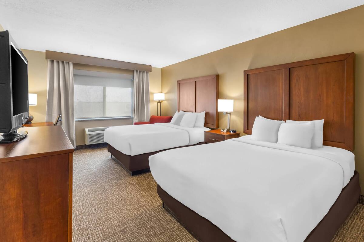 A hotel room with two beds, a desk, a TV, and a window with curtains.
