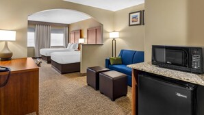 A hotel room with a bed, two bedside tables, a desk with a telephone, a microwave, a refrigerator, a sofa, and a small table with a lamp.