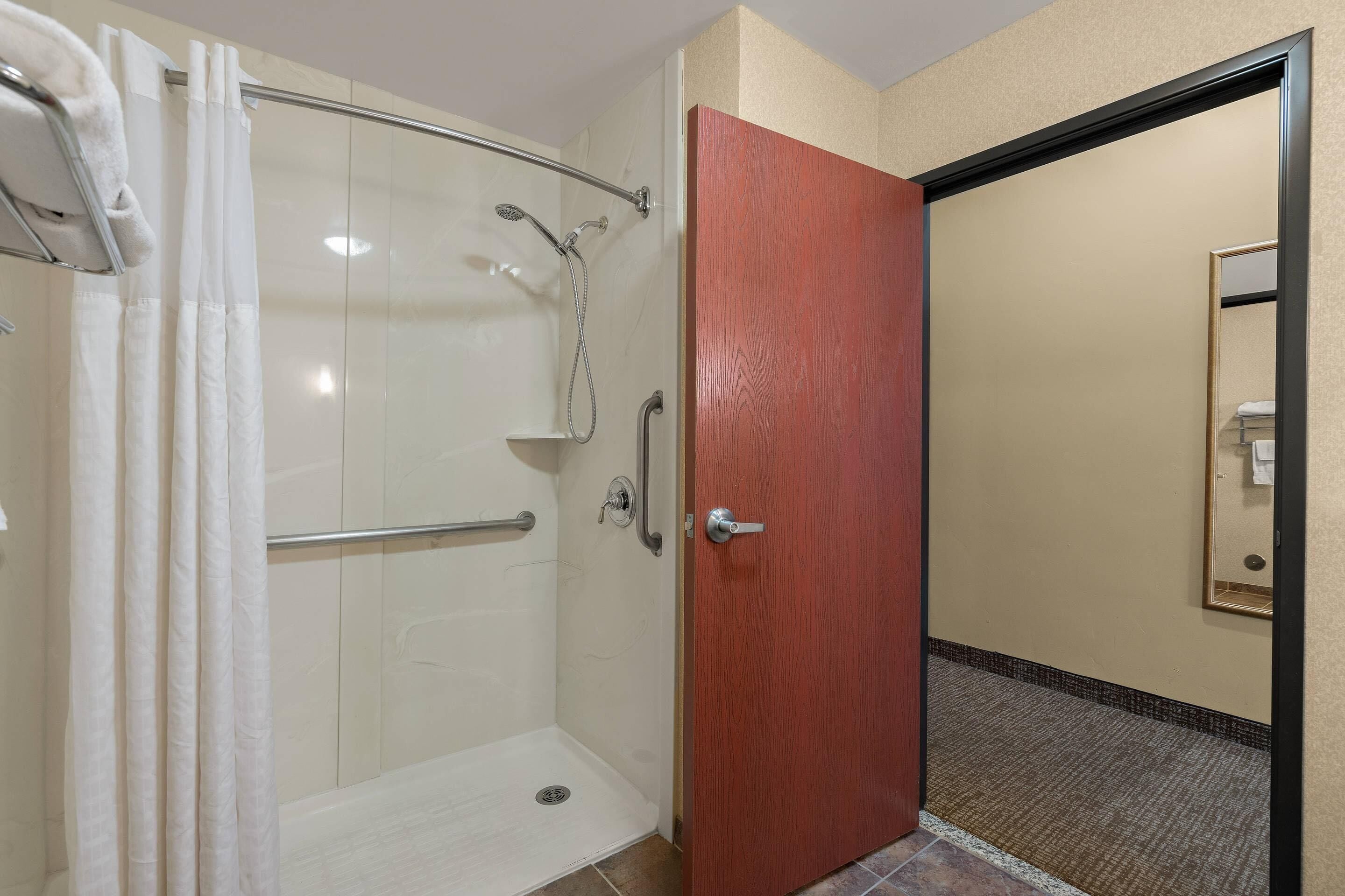 A hotel bathroom with a shower, a door, and a mirror.