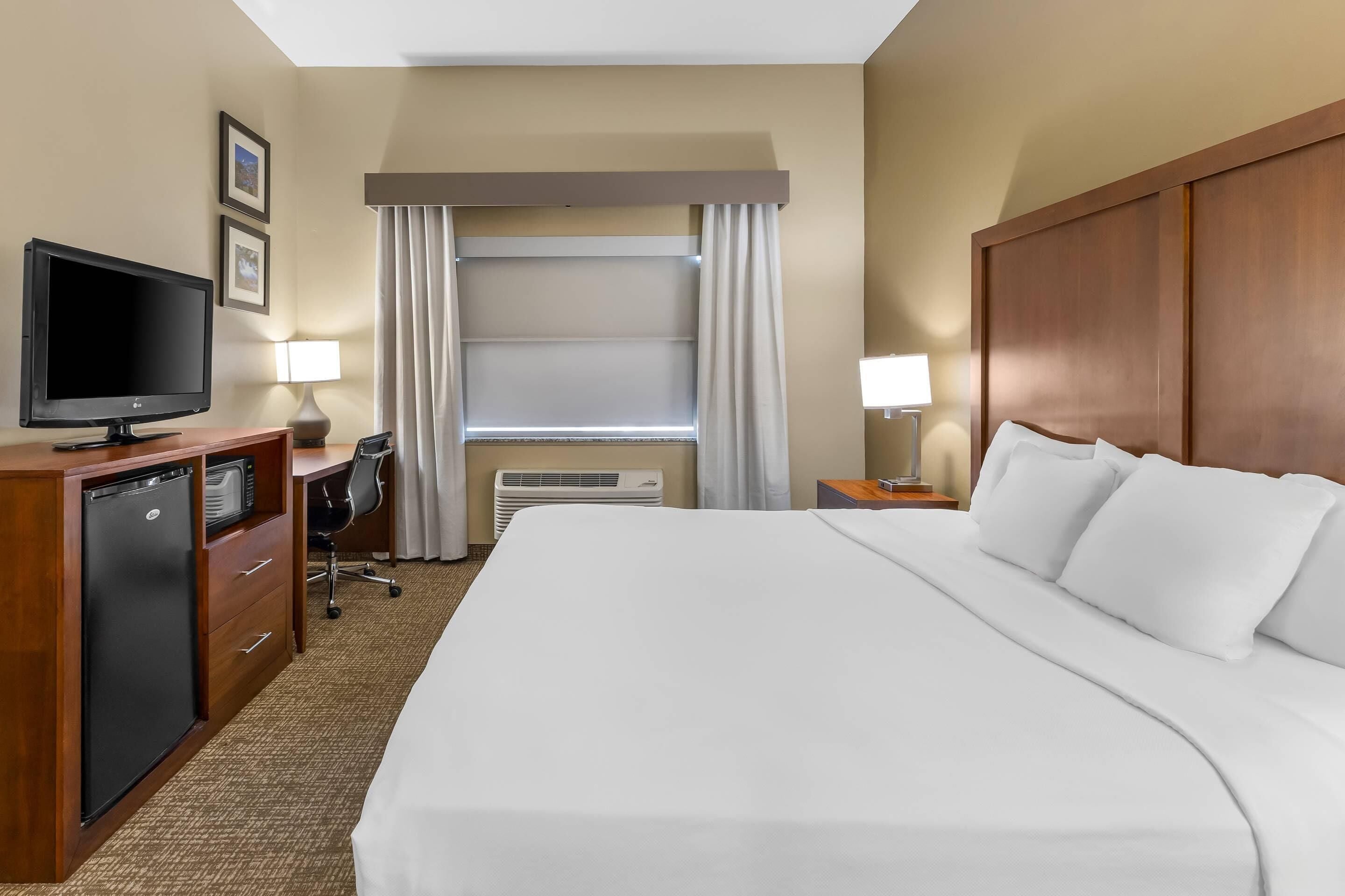 Habitación de hotel con una cama grande, televisión, escritorio con computadora, una silla y ventana con cortinas.