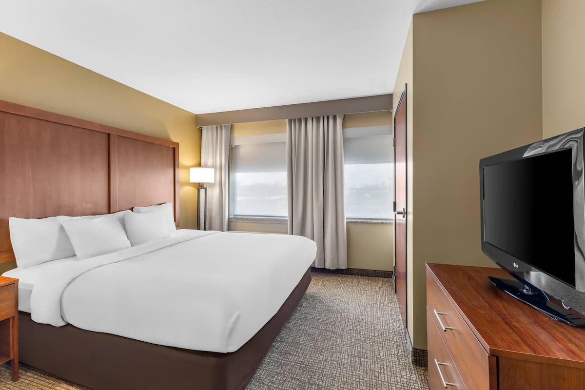 A hotel room with a large bed, a TV on a wooden dresser, and a window with curtains.