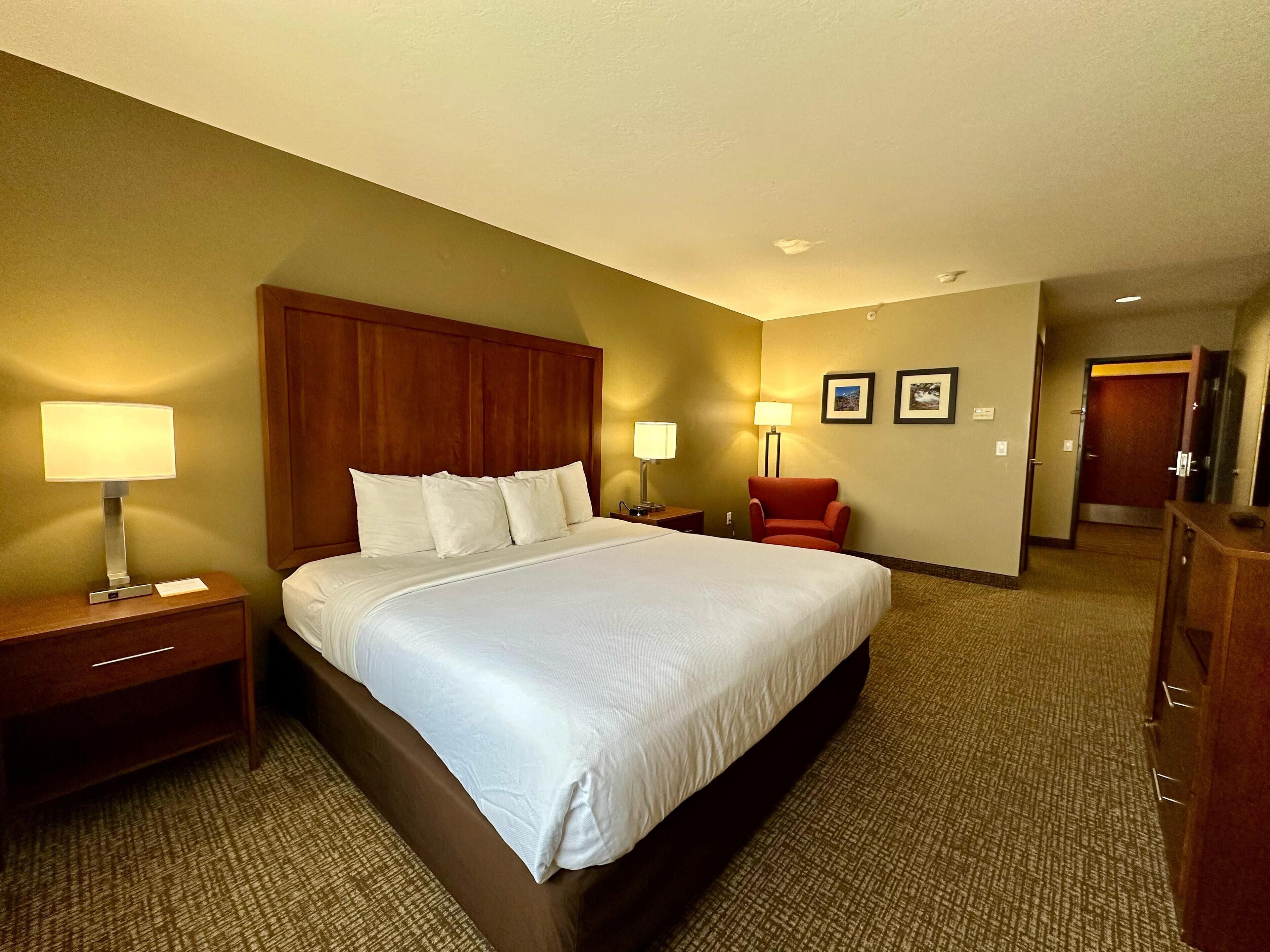 A hotel room with a large bed, two bedside lamps, a chair, and a desk with a lamp.