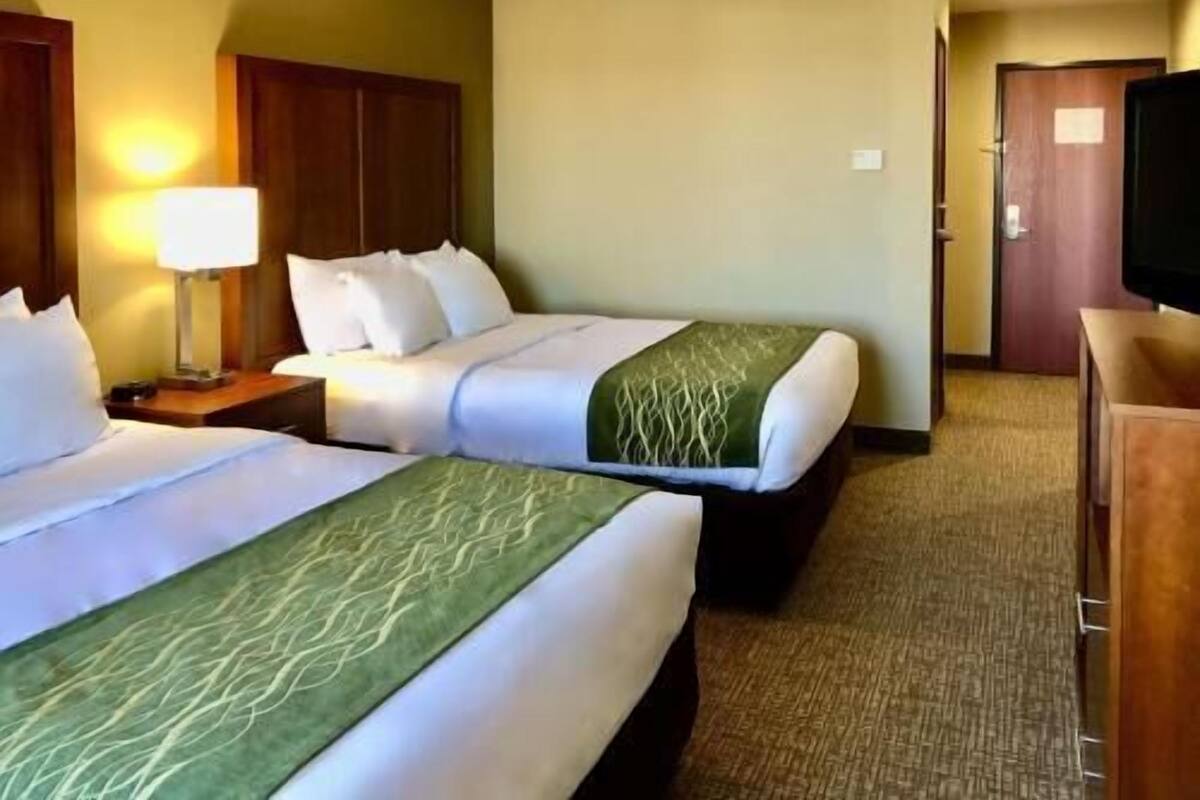 A hotel room with two beds, a TV, a lamp, and a wooden cabinet.