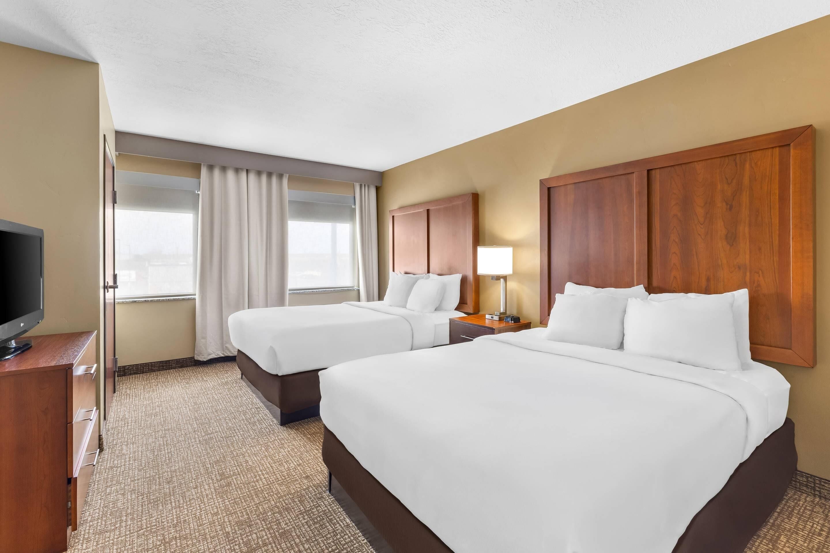 A hotel room with two beds, a television, a desk, and a window with curtains.