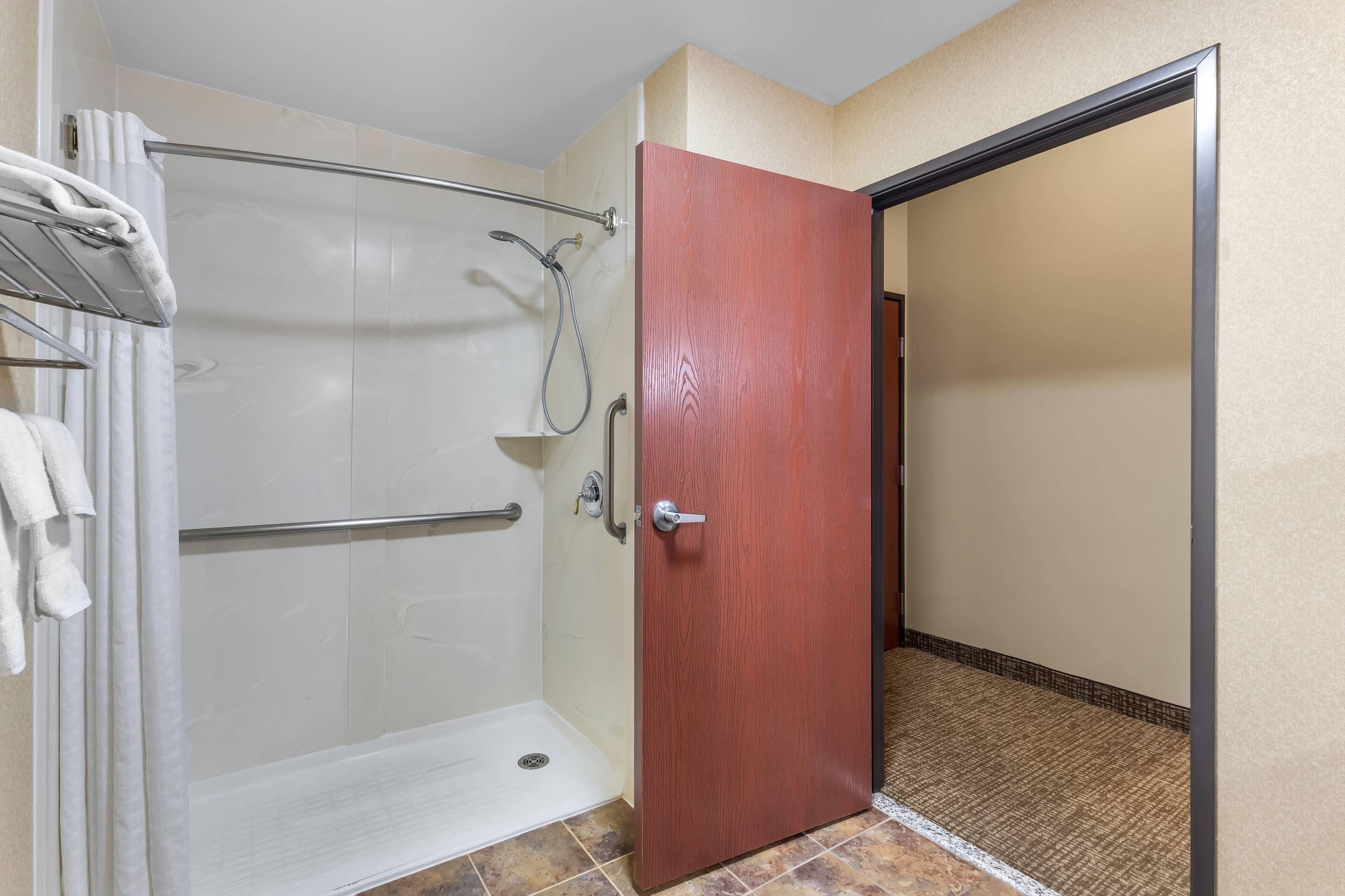 A bathroom with a shower, a towel rack, and a wooden door.