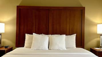 A neatly made bed with white linens and pillows, a wooden headboard, and two bedside tables with lamps.
