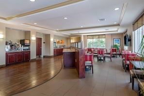 Een ruime hotellobby met een houten vloer, een receptiebalie en een zithoek met rode en witte stoelen.