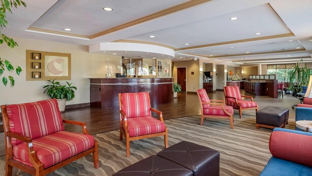 A hotel lobby with a reception desk, seating areas, and a kitchen in the background. - Comfort Suites Biloxi - Ocean Springs (Biloxi)