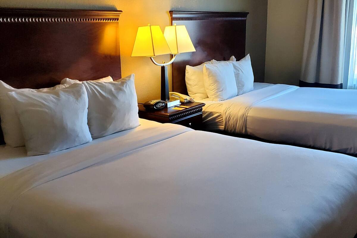 Una habitación de hotel con dos camas, una mesita de noche con lámpara y un teléfono.