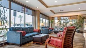 A spacious lobby with large windows, a blue sofa, a wooden chair, and a patterned carpet. - Comfort Suites Biloxi - Ocean Springs (Biloxi)