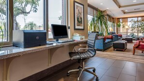 A hotel reception area with a desk, computer, chair, sofa, and potted plants. - Comfort Suites Biloxi - Ocean Springs (Biloxi)