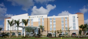A multi-story hotel with a clear sky, palm trees, and a sign reading "HYATT PLACE".
