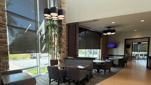 A modern restaurant with large windows, indoor plants, and a variety of seating options. - Hyatt Place Fort Myers/at The Forum (Fort Myers)