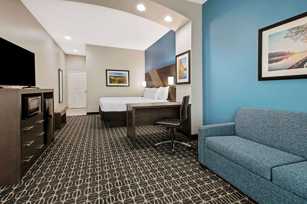Une chambre d’hôtel équipée d’un lit, d’un bureau, d’une chaise, d’un canapé, d’une télévision et d’œuvres d’art accrochées aux murs.
