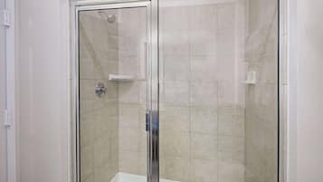 A glass-enclosed shower area with a white bathtub.