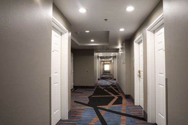 Un pasillo de hotel con pisos alfombrados, puertas blancas e iluminación empotrada.