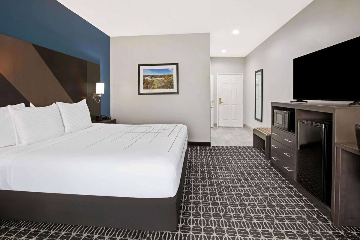 Une chambre d’hôtel avec un grand lit, un bureau doté d’un téléviseur à écran plat, une porte et un tableau encadré au mur.