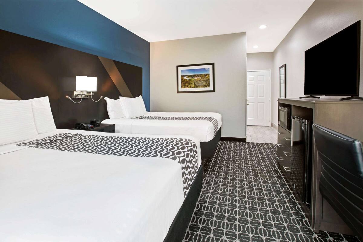 Une chambre d’hôtel avec deux lits, un téléviseur à écran plat, un bureau avec une chaise et un tableau au mur.