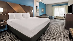 Habitación de hotel con una cama grande, un escritorio, una silla, un televisor y un ventanal con cortinas.