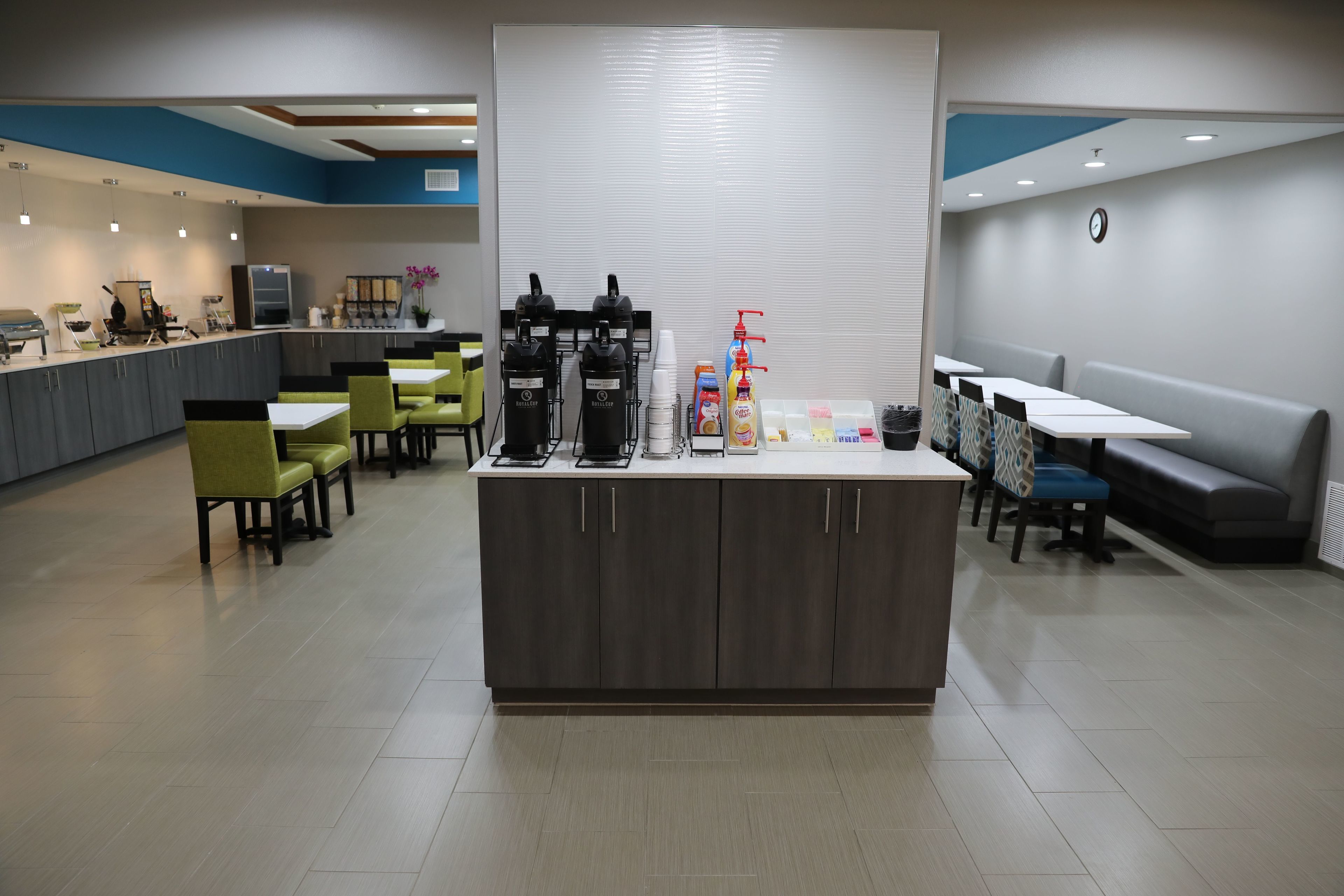 A modern cafe with a central counter, seating area, and a clock on the wall.