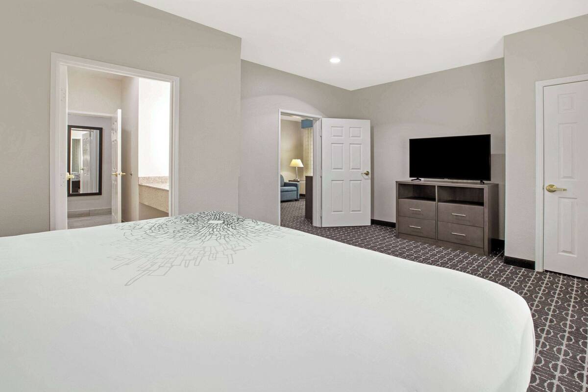 Une chambre d’hôtel avec un grand lit, une télévision, une commode et une porte donnant sur une autre pièce.