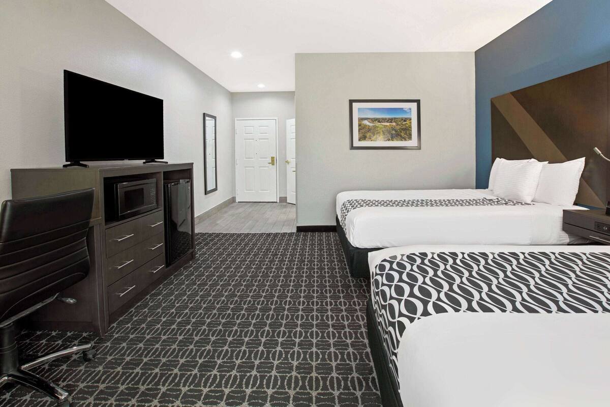 Une chambre d’hôtel avec deux lits, un bureau doté d’un téléviseur à écran plat, un four à micro-ondes et une porte donnant sur un couloir.