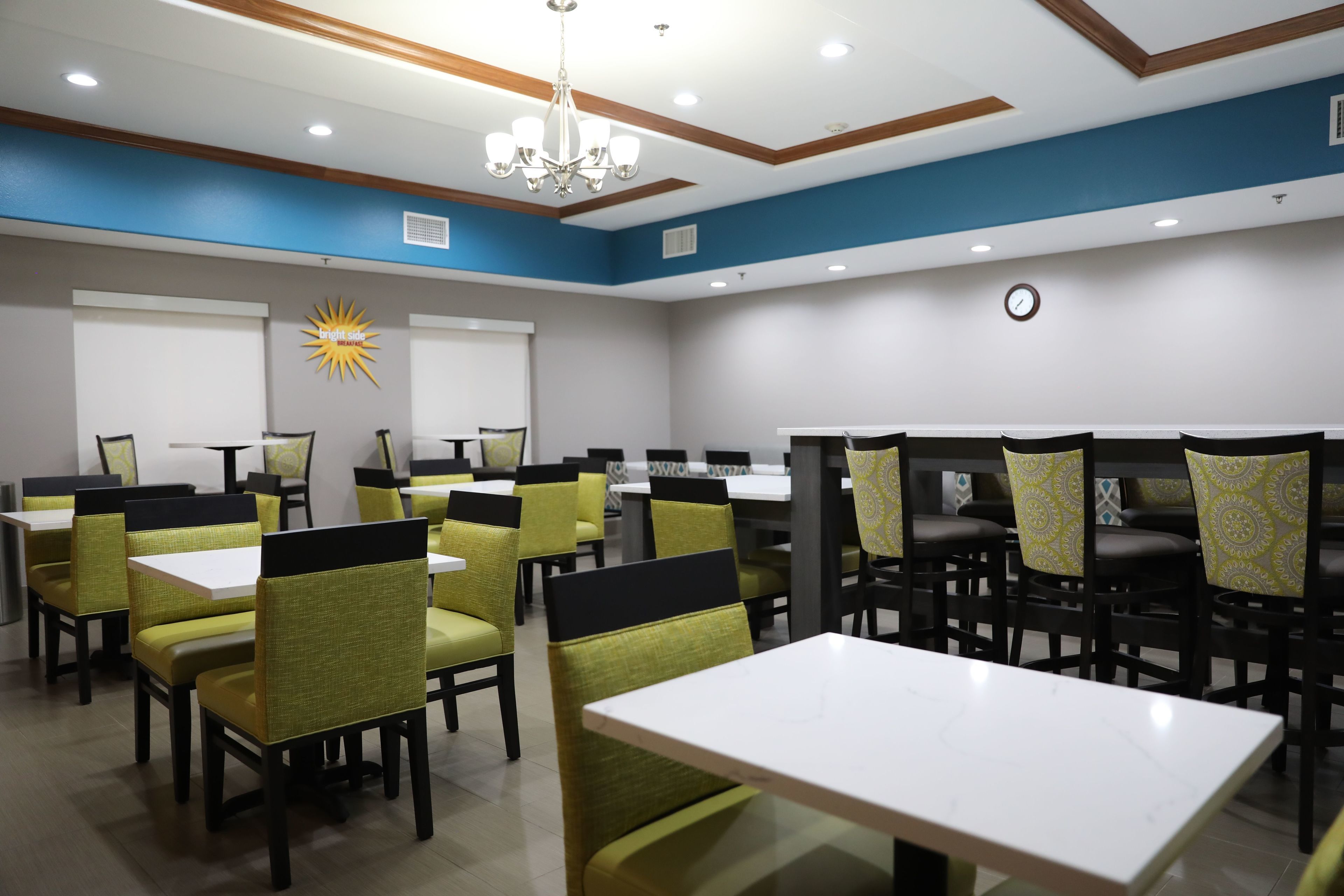 A dining area with tables and chairs, a chandelier, and a clock on the wall.