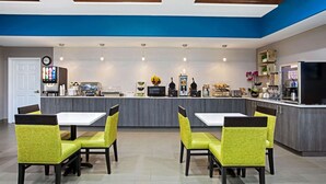 Una cocina moderna con gabinetes grises, una isla central y un comedor con sillas amarillas y mesas blancas.