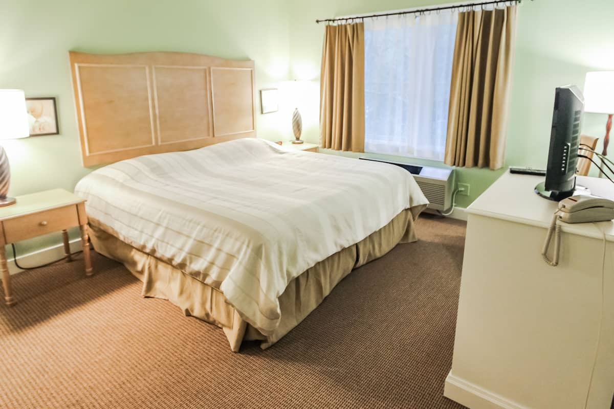 A hotel room with a large bed, a desk with a telephone, a television, and a window with curtains.