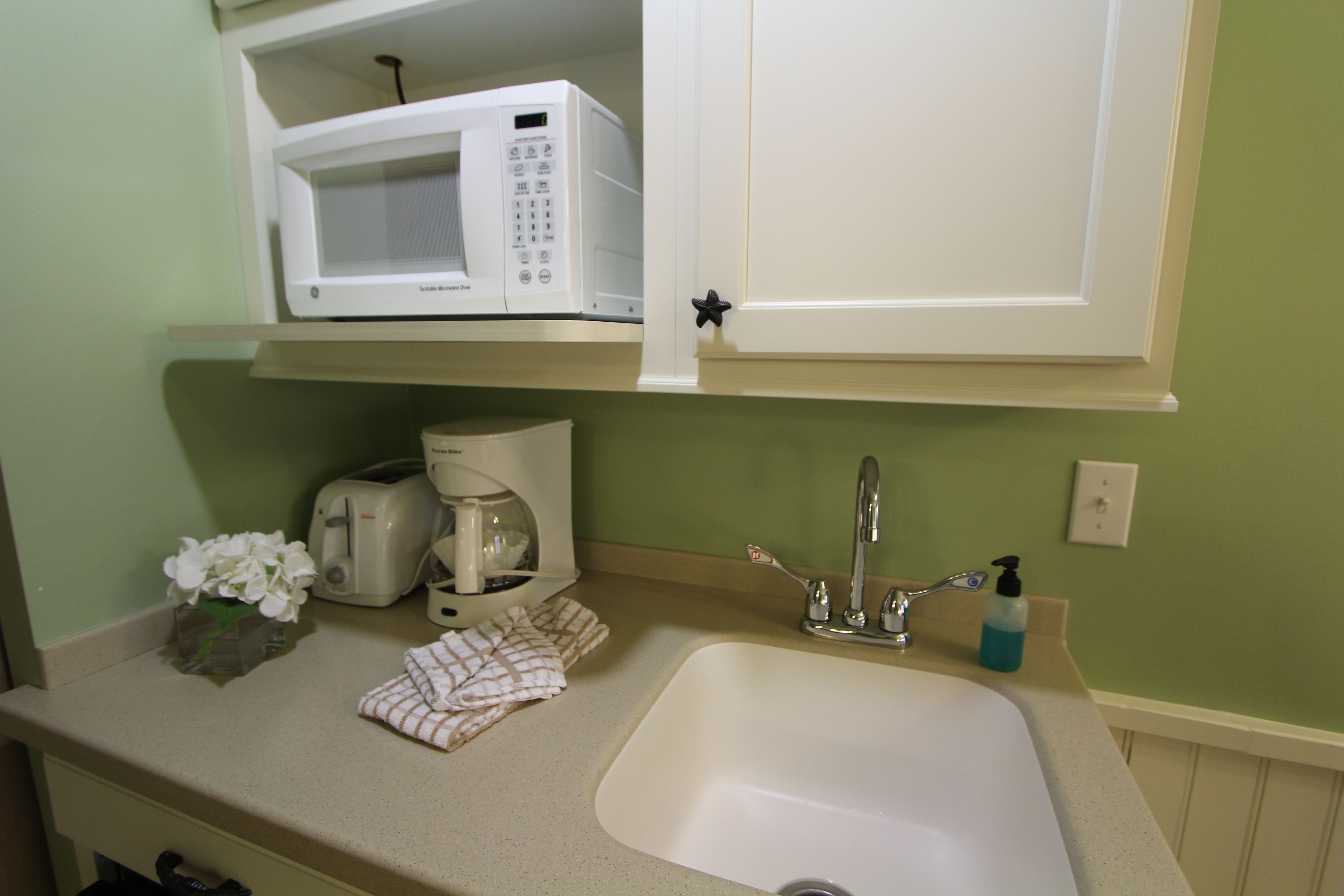 A kitchen with a microwave, toaster, sink, and a bottle of hand soap.